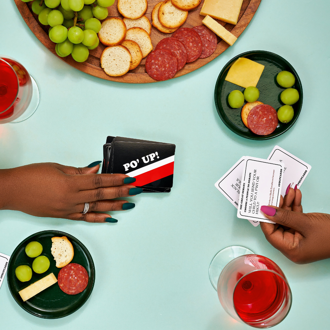 PO' UP! Card Game against a blue backdrop on a table with charcuterie and glasses of wine displayed next to cards