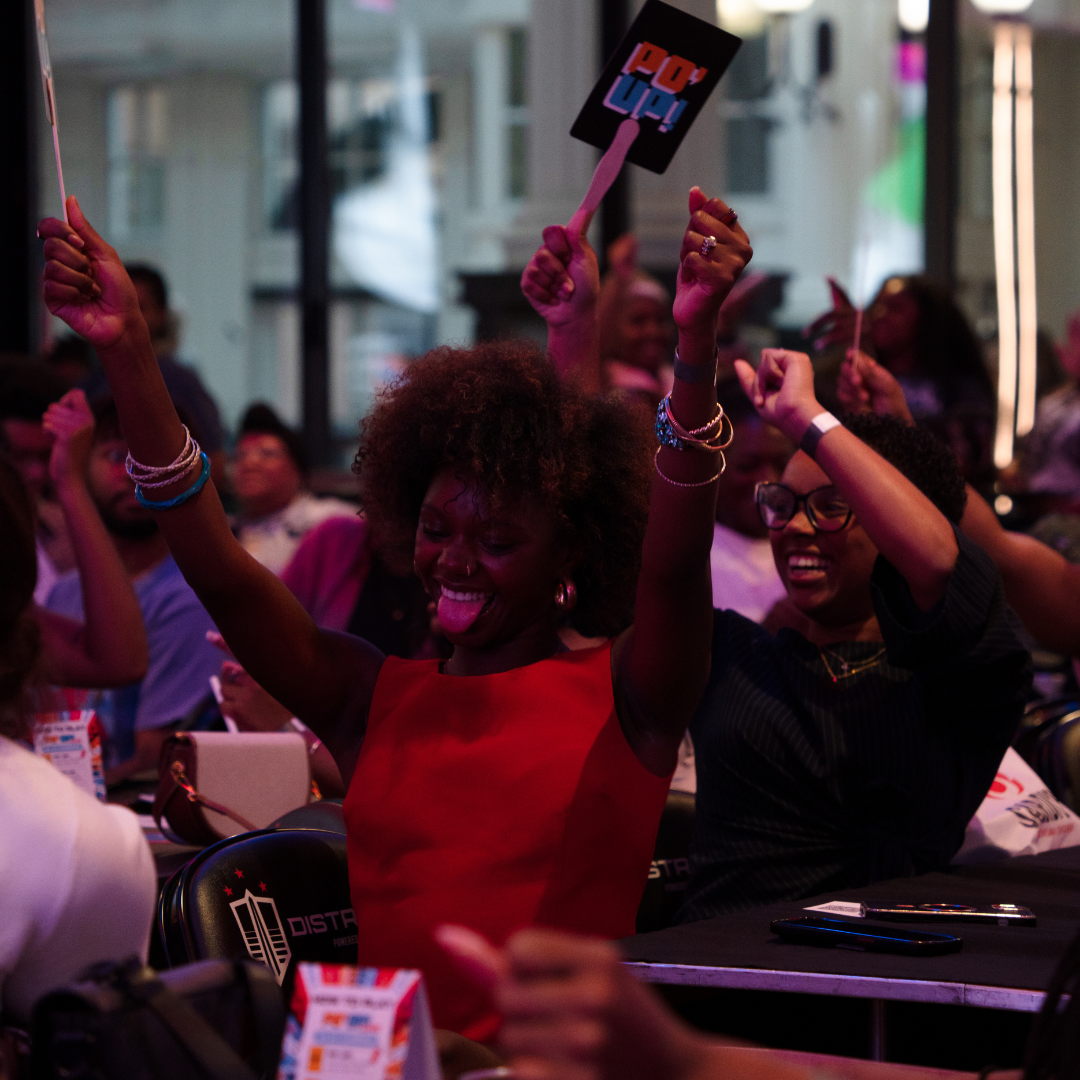 Audience members waving red and black church fans labeled "PO' UP!" as they play along during PO' UP! Live, our live game show.